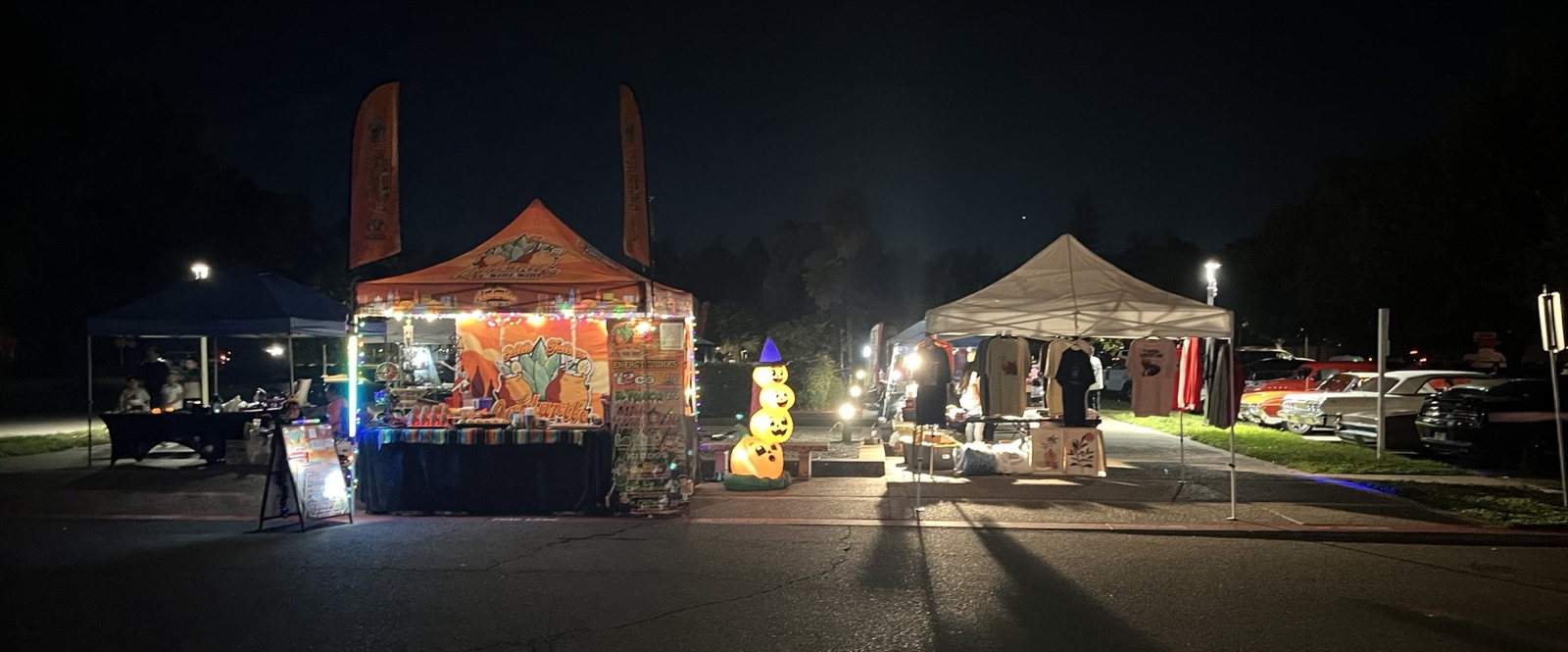 Classic cars and lowriders lined up with vendor tents at the night car show